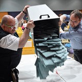 Zwei Männer schütten Stimmzettel aus einer Wahlurne auf einen Tisch