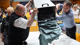 Zwei Männer schütten Stimmzettel aus einer Wahlurne auf einen Tisch