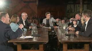 Moderator Felix Krömer sitzt mit Bremer Spitzenpolitikern an einem großen Tisch und diskutiert