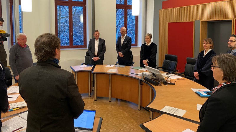 Die Mitglieder des Bremer Wahlprüfungsgericht stehen im Kreis an ihren Tischen.