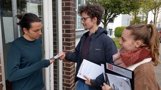 Zwei Wahlscouts sprechen mit einem Mann an einer Haustür.