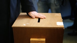 Ein Mann legt seine Hand auf den Schlitz einer Wahlurne (Archivbild)