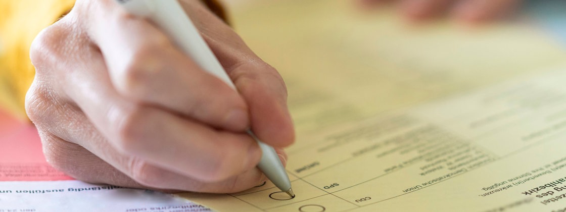 Nahaufnahme einer Hand mit Stift beim Ausfüllen des Wahlzettels