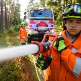Ein Feuerwehrmann löscht mit einem Schlauch in einem Waldstück