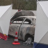 Ein ausgebranntes Auto wird von einer Plane verdeckt.