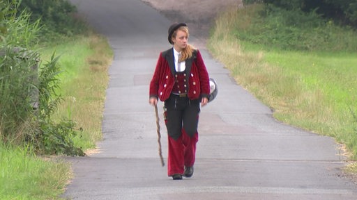 Die Wandergesellin Helene Steinberg läuft mit einem Wanderstock eine Straße entlang.