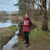 Eine Frau steht mit einem Wanderführer an einem See.