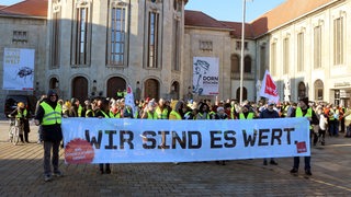 Eine Gruppe Demonstranten steht mit einem Banner vor einem Gebäude.