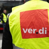 Ein Mensch in Warnweste mnit "Verdi"-Logo steht mit anderen vor einem Linienbus.