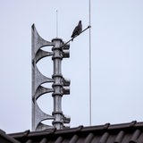Eine Taube sitzt auf einer elektronischen Sirene, die auf dem Dach eines Hauses installiert ist.