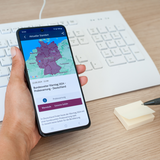 Handy vor Tastatur mit Deutschlandkarte und Warnmeldung.