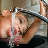 Ein Mädchen trinkt Leitungswasser aus einem Wasserhahn.