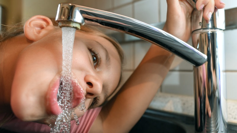 Ein Mädchen trinkt Leitungswasser aus einem Wasserhahn.