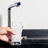 Ein Mann füllt ein Wasserglas unter einen Wasserhahn.