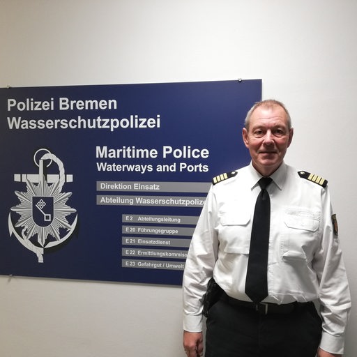 Ein Mann in Polizeiuniform steht vor einem Schild der Wasserschutzpolizei Bremen 