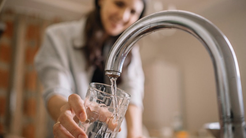 Eine Frau lässt Wasser aus einem Wasserhahn in ein Glas laufen