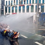 Menschen sitzen auf der Straße und werden von zwei Wasserwerfern getroffen.