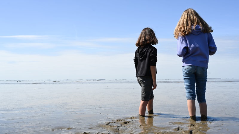 Zwei Mädchen sind Barfuß im Wattenmeer unterwegs und genießen das Wetter.