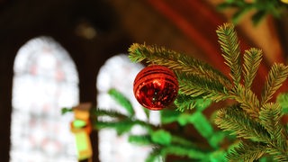 Eine rote Kugel an einem Weihnachtsbaum, im Hintergrund sind Kirchenfenster zu sehen.