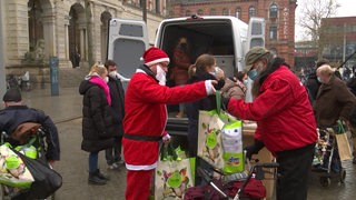 Eine Person verkleidet als Weihnachtsmann verteilt Spenden an Bedürftige.