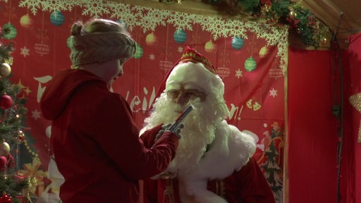 Der Bremer Weihnachtsmarkt hat einen neuen Weihnachtsmann. Neben ihm ein Kind mit Schokolade in den Händen.