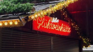 Ein Neonschild einer Weihnachtsmarkt-Bude, auf dem Glühweinhütte steht.
