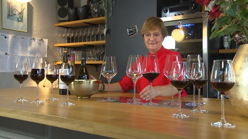 Die Weinhändlerin Andrea Dehn, umgeben von mehreren gefüllten Weingläsern in ihrer Weinmühle. 
