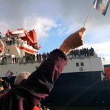 Menschen mit Fahnen begrüßen ein Schiff