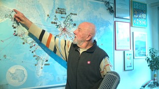 Ein Mann steht vor einer Weltkarte und zeigt mit dem Finger auf Nordamerika.