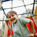 Ein lachender Junge turnt in einem Klettergerät auf einem Spielplatz