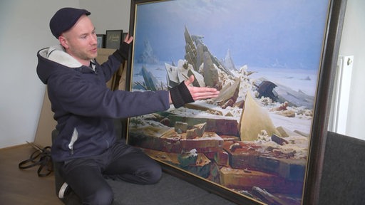 Zu sehen ist der Künstler Julian Hölscher, wie er eines seiner Bilder zeigt.