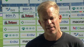 Werder-Trainer Markus Anfang beim Interview vor einer Werbewand.