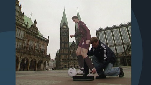 Eine Person stellt einen Aufsteller eines Fußballspielers auf dem Bremer Marktplatz auf.