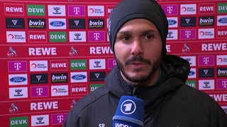 Werder-Spieler Leonardo Bittencourt ernüchtert nach dem Spiel in Köln beim Interview vor einer Werbewand.