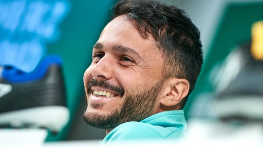 Werder-Spieler Leonardo Bittencourt mit einem breiten Lächeln während einer Pressekonferenz.