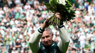 Frank Baumann applaudiert mit einem Blumenstrauß in den Händen