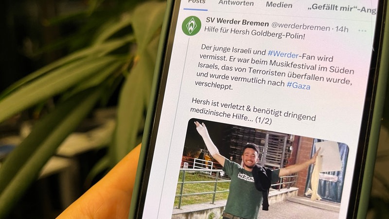 Ein Handydisplay zeigt einen Post von Werder Bremen auf X, auf dem zur Suche nach einem Fan aufgerufen wird.