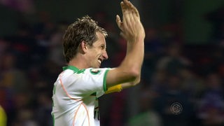 Werder Bremens Fußballspieler freut sich und klatscht mit den Händen auf dem Spielfeld.