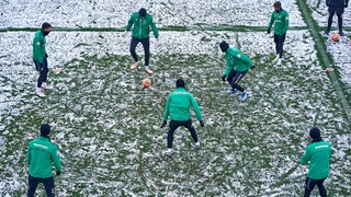 Die Werder-Spieler spielen sich auf von Schnee bedecktem Platz im Training den Ball zu.