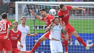 Zwei hochspringende Heidenheim-Spieler nehmen Werder-Verteidiger Marco Friedl in die Zange.