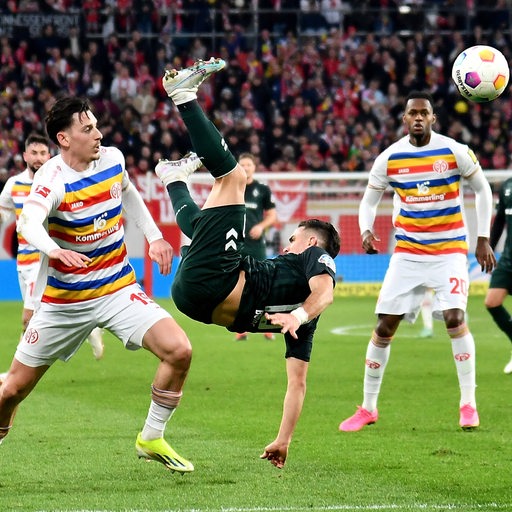 Werder-Angreifer Rafale Borre liegt quer in der Luft, während sein Gegenspieler dem Ball nachschaut.