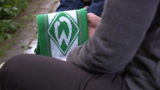 Es ist eine Person zu sehen, welche einen Werder Bremen Schal in der Hand hält.