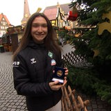 Eine Frau mit einer Medaille in der Hand lächelt in die Kamera.