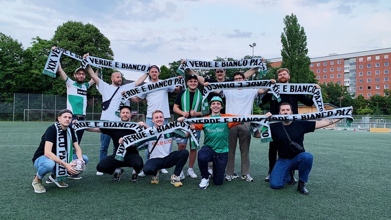 Die Mitglieder des Werder-Fanclubs "Verde e Bianco Pazzo" halten ihre Fanschals in die Höhe.