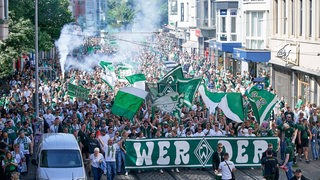 Werder-Fans marschieren zum Weser-Stadion und schwenken Fahnen.