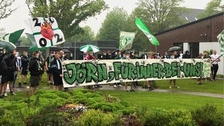 Werder-Fans halten ein Banner mit der Aufschrift "Jörn, für immer bei uns!" hoch, schwenken Werder-Fahnen und singen dabei Fanlieder der Bremer.