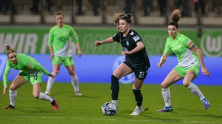 Zwei Fußballerinnen - eine Wolfsburgerin im grünen Trikot und eine Bremerin im schwarzen Trikot - kämpfen um den Ball.