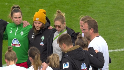 Die Mannschaft der Werder Frauen auf dem Spielfeld zusammen mit dem Trainer.