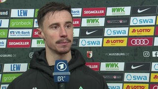Werder-Kapitän Marco Friedl steht vor einer Werbewand beim Interview nach dem Spiel.