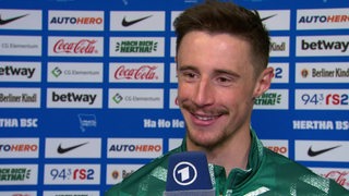 Werder-Kapitän Marco Friedl lächelt vor einer Werbewand beim Interview nach dem Spiel.